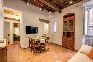 A dining area with a wooden table and chairs, a television mounted on the wall, and a cabinet with glass doors. - Charming Roman Home Just Steps from Campo de' Fiori (Roma)