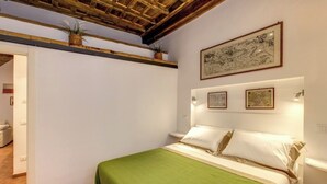 Ein Schlafzimmer mit einem Bett, einer grünen Bettdecke, einer Holzbalkendecke und gerahmten Kunstwerken an der Wand.
