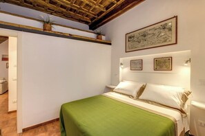 Ein Schlafzimmer mit einem Bett, einer grünen Bettdecke, einer Holzbalkendecke und gerahmten Kunstwerken an der Wand.