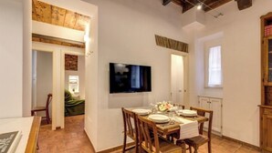 Ein Essbereich mit Holztisch, gedeckt für vier Personen, einem an der Wand befestigten Flachbildfernseher und Blick in einen Raum mit einem grünen Sofa.