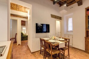 Ein Essbereich mit Holztisch, gedeckt für vier Personen, einem an der Wand befestigten Flachbildfernseher und Blick in einen Raum mit einem grünen Sofa.