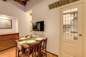 A dining area with a table set for four, a television mounted on the wall, and a door with a frosted glass panel. - Charming Roman Home Just Steps from Campo de' Fiori (Roma)