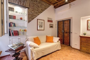 A cozy living room with a white sofa, a bookshelf, and a wooden door. - Charming Roman Home Just Steps from Campo de' Fiori (Roma)