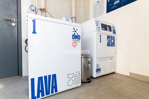 Deux machines à laver blanches, ornées de logos bleus et blancs, avec une porte en métal et un panneau fixé au mur.