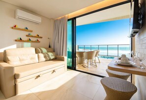 A modern living room with a sofa, a dining table with chairs, and a view of the ocean through a glass door. - Vila Porto by Carpediem In Front of Porto de Galinhas Beach (Ipojuca)