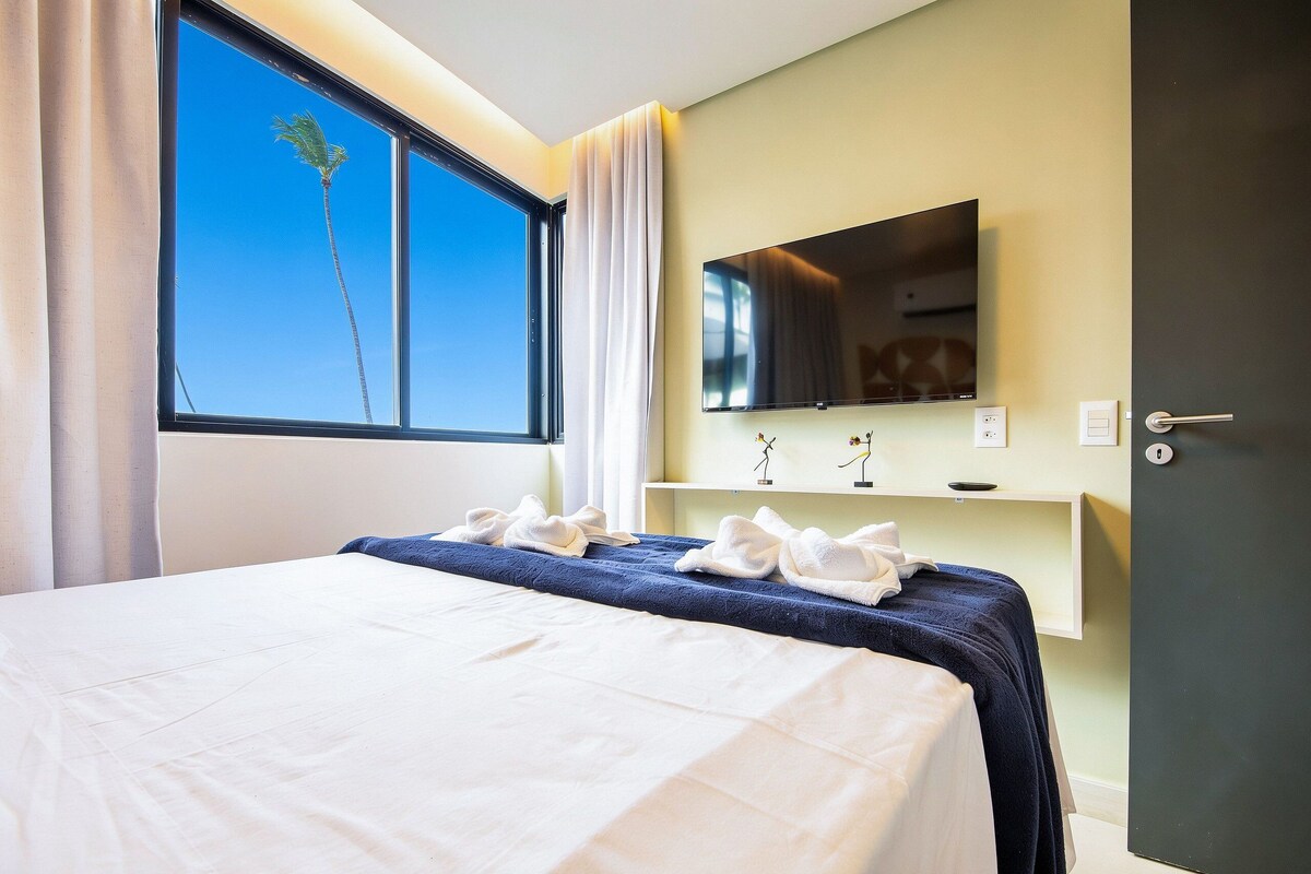 A hotel room with a bed, a TV, a mirror, and a window with curtains.