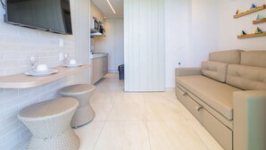 A modern kitchen with a flat-screen TV, a dining area with stools, and a sofa. - Vila Porto by Carpediem In Front of Porto de Galinhas Beach (Ipojuca)