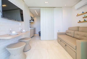 A modern kitchen with a flat-screen TV, a dining area with stools, and a sofa. - Vila Porto by Carpediem In Front of Porto de Galinhas Beach (Ipojuca)