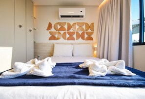 Una camera d'albergo con un letto, cuscini bianchi, una coperta blu e un condizionatore d'aria a parete.