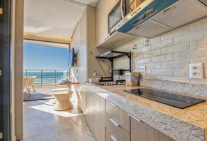 A modern kitchen with a view of the ocean, a built-in stove, and a dining area with wicker chairs. - Vila Porto by Carpediem In Front of Porto de Galinhas Beach (Ipojuca)