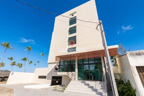 Un hotel moderno con un ingresso ben visibile, una scala che conduce alla hall e una vista aperta sulle palme circostanti.