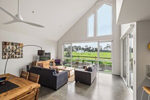 A modern living room with a dining area, large windows, and a view of a green landscape.