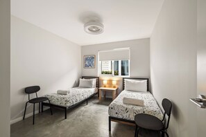 Ein kleines, modernes Schlafzimmer mit zwei Einzelbetten, einem Schreibtisch und einem Stuhl.