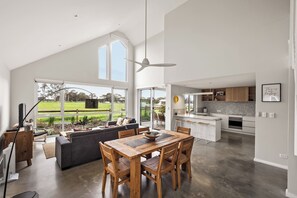 A spacious living area with a dining table and chairs, a sofa, and a view of a garden through large windows.