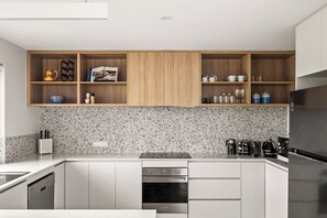 A modern kitchen with white cabinetry, a granite countertop, and a built-in oven. - Karrack House - Peaceful family holiday home in Witchcliffe Ecovillage (Witchcliffe)