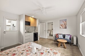 Un dormitorio moderno con cama, sofá, una mesita redonda y kitchenette.