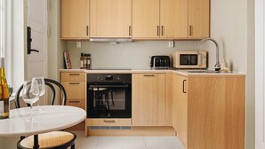 A compact kitchen with wooden cabinets, a built-in oven, a microwave, and a dining area with a table and chairs. - 500m to Bryggen • Renovated 2025 • Bathtub Bliss! (Bergen)