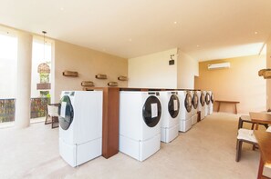 A laundry room with multiple washing machines arranged in a row. - Cozy 1-bedroom condo in serene Tulum with AC, pool, gym access and bikes (Tulum)