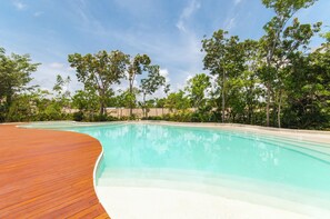 Ein klares Schwimmbecken mit Holzterrasse an einer Seite und sandigem Beckenboden.