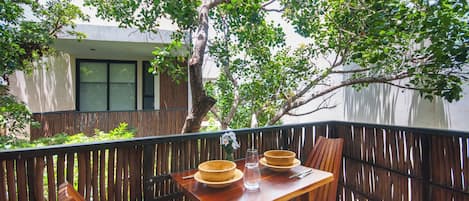A wooden table with a bowl and a glass on it, set on a balcony with a view of a tree and a building.