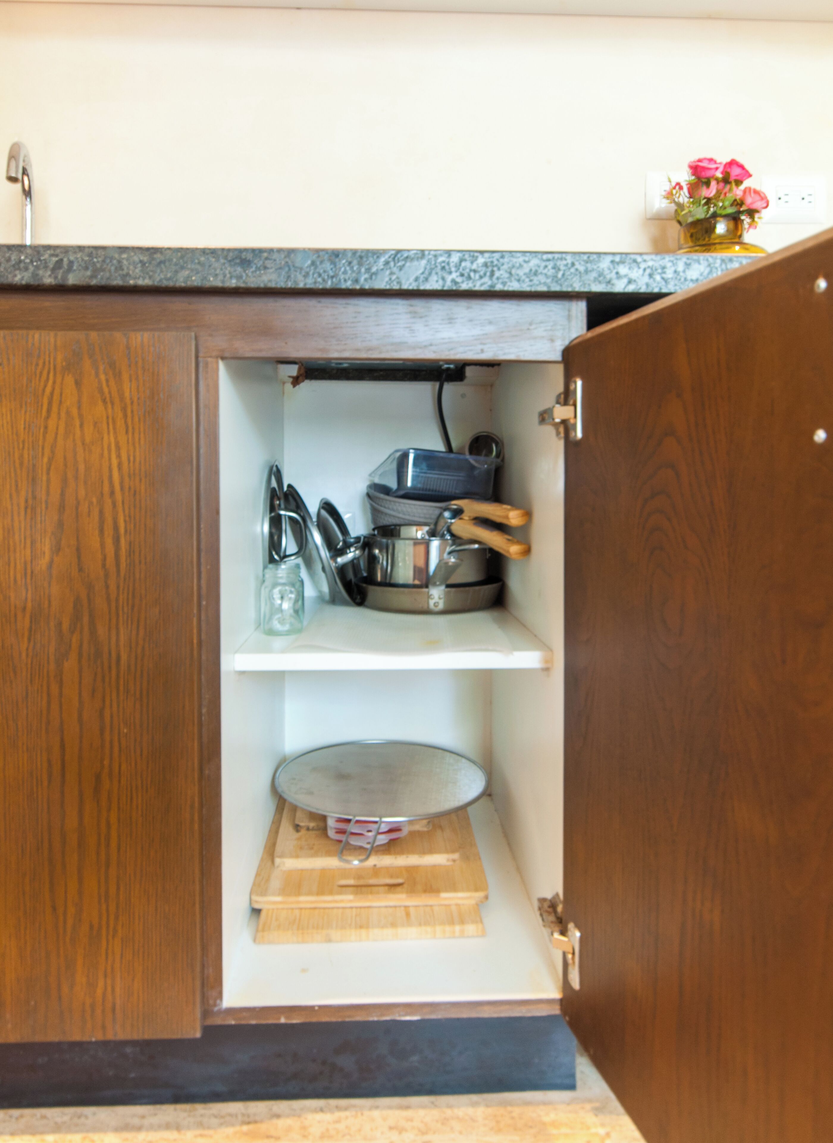 A kitchen cabinet with a wooden interior, a metal pot, a plastic container, and a wooden cutting board.