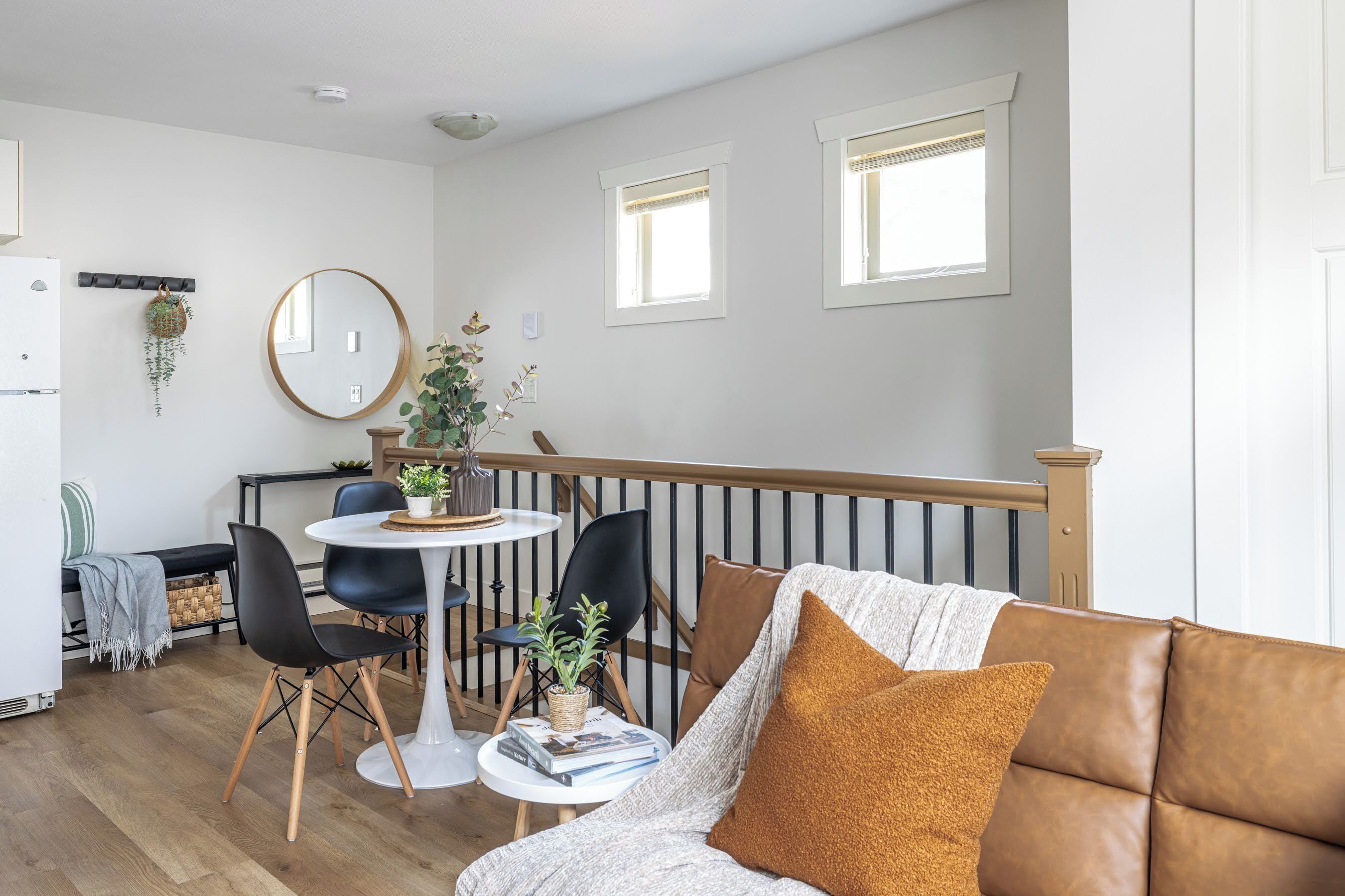 A modern living room with a brown leather sofa, a round table with chairs, and a dining area with a white table and chairs.