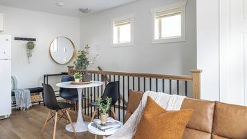 A modern living room with a brown leather sofa, a round table with chairs, and a dining area with a white table and chairs.