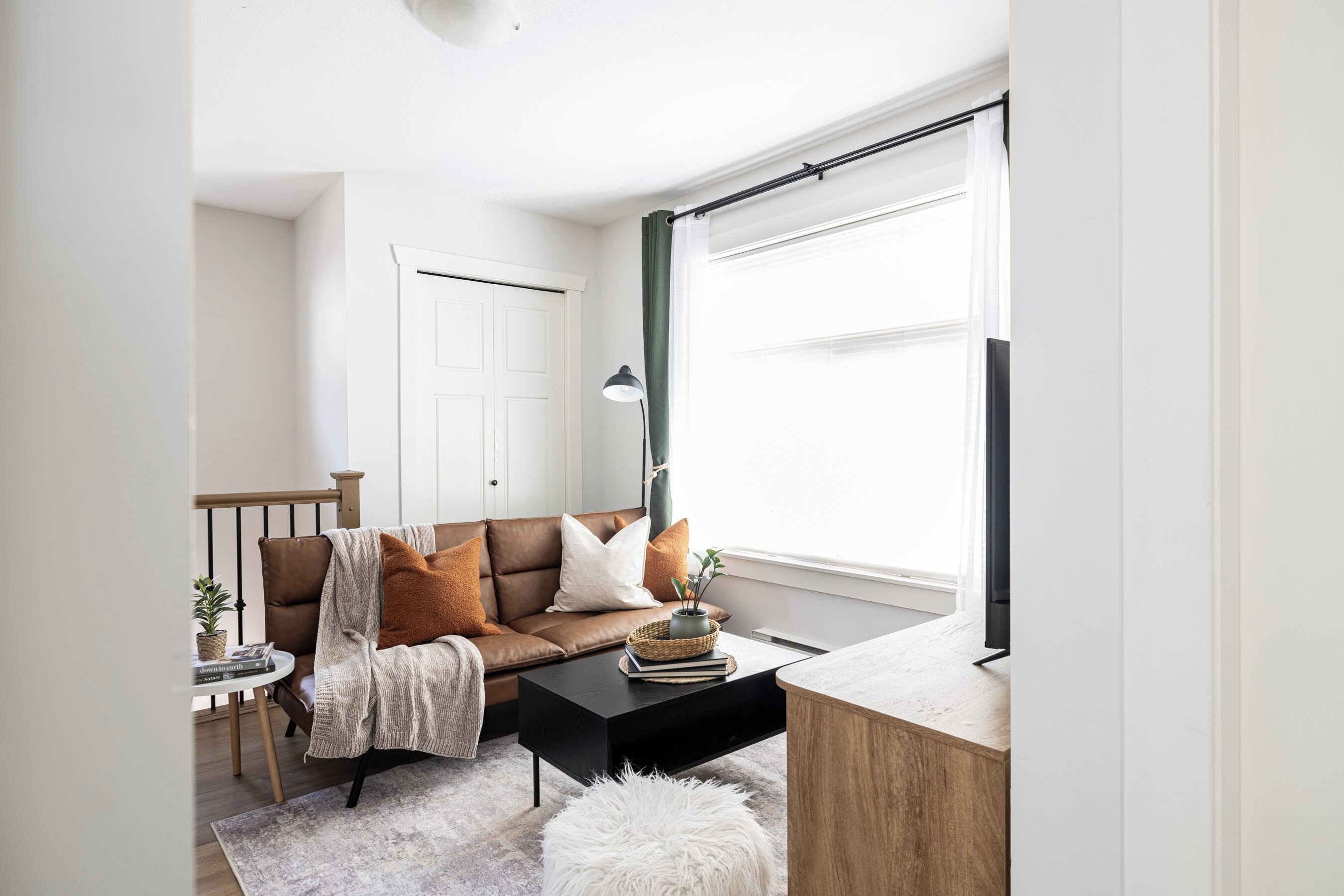 Een moderne woonkamer met een bruine leren bank, een zwarte salontafel, een witte vloerlamp en een houten bijzettafeltje met een plant.