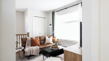 Een moderne woonkamer met een bruine leren bank, een zwarte salontafel, een witte vloerlamp en een houten bijzettafeltje met een plant.