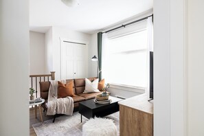 A modern living room with a brown leather sofa, a black coffee table, a white floor lamp, and a wooden side table with a plant. - Suburban Escape - Coach House (Surrey)