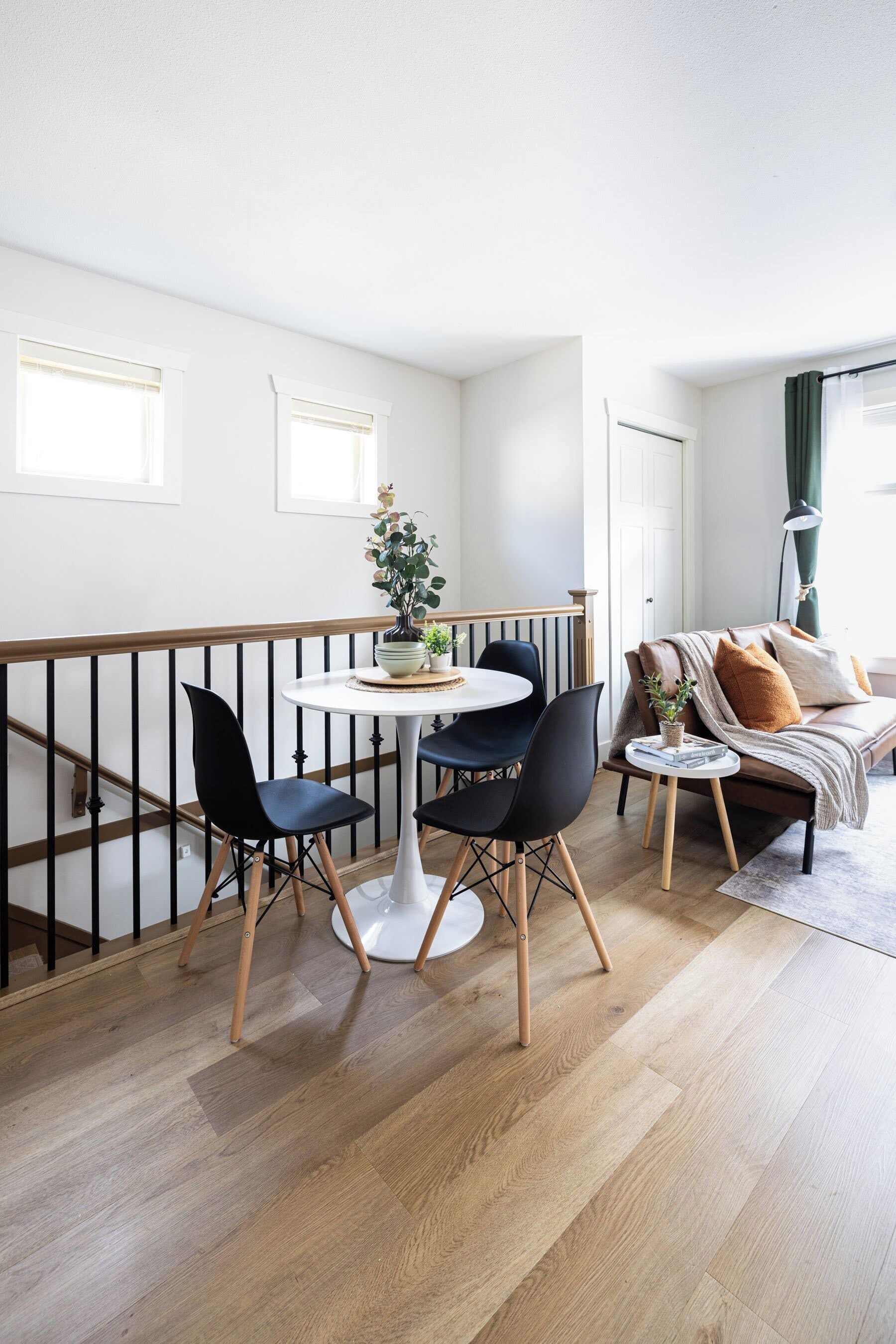 Una sala de estar moderna con comedor, piso de madera y un balcón con barandilla.