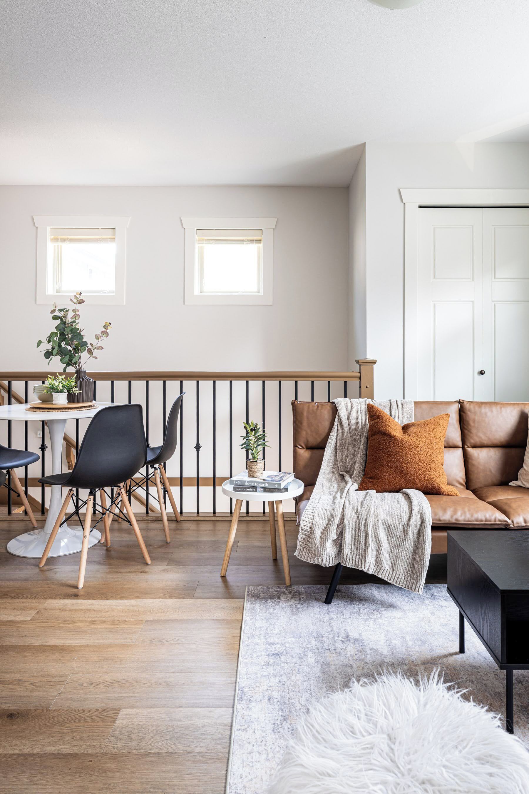 A modern living room with a brown leather sofa, a white rug, and a dining area with a table and chairs.
