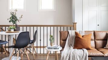 A modern living room with a brown leather sofa, a white rug, and a dining area with a table and chairs.