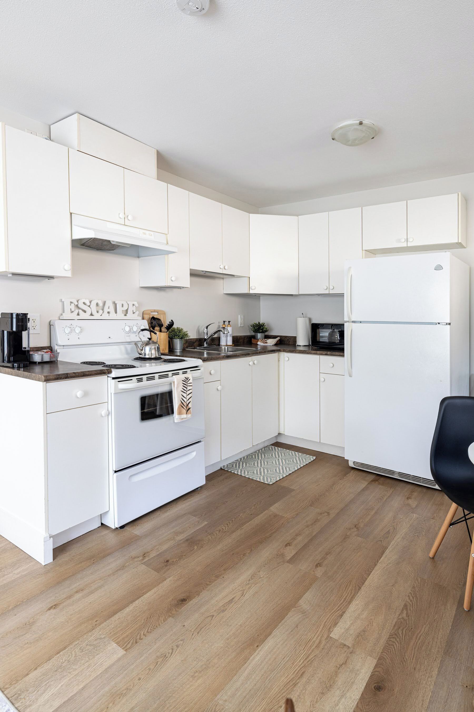 Una cocina moderna con armarios blancos, estufa, refrigerador y piso de madera.