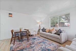 Een woonkamer met een eettafel, bank en een groot raam met zonwering.