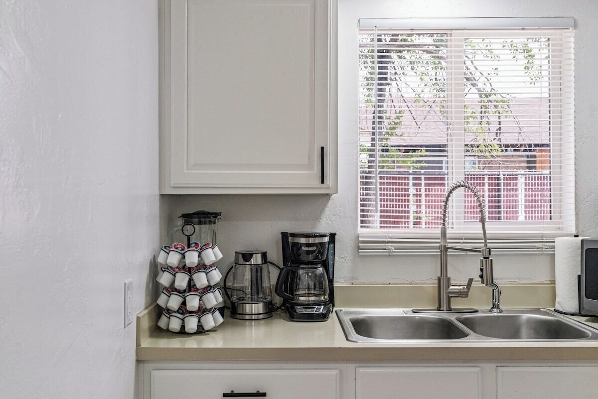 A kitchen with a double sink, a coffee maker, and a window with blinds.