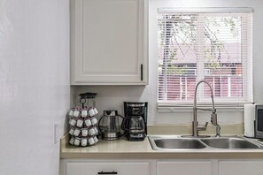 Een keuken met een dubbele spoelbak, een koffiezetapparaat en een raam met jaloezieën.
