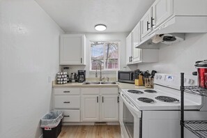 A compact kitchen with white cabinets, a stove, a microwave, and a sink.