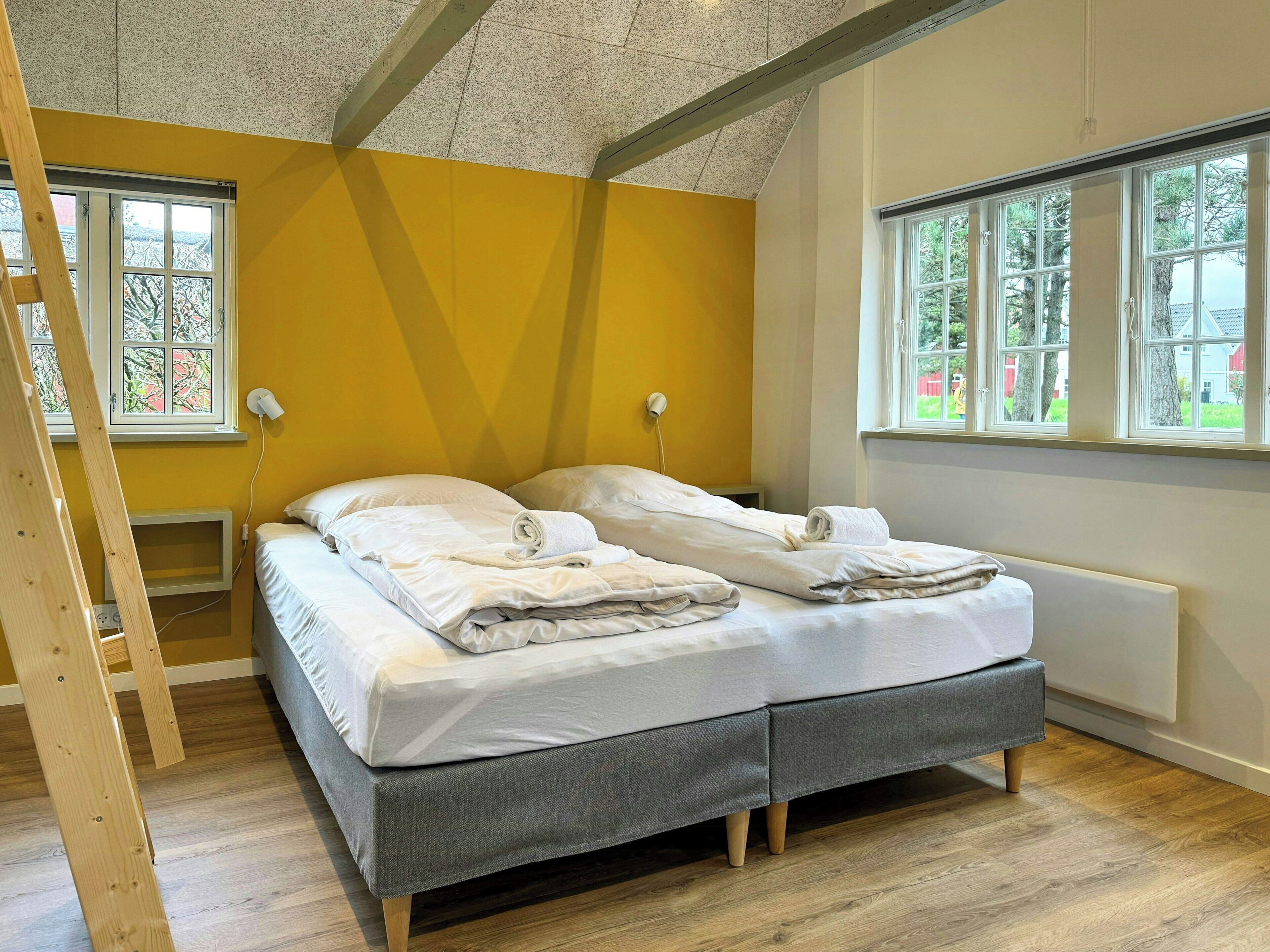 A room with a bed, a ladder, and large windows.