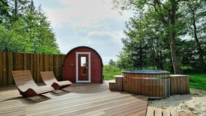 Una terraza de madera con sillones, una bañera de hidromasaje y un edificio rojo con una puerta.