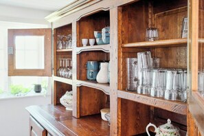 Een houten kast met planken, gevuld met divers glazen servies en keramieken voorwerpen.