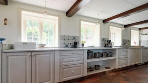 Una cocina con armarios blancos, salpicadero de azulejos y piso de baldosas de piedra.