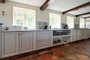 A kitchen with white cabinetry, a tiled backsplash, and a stone tile floor. - Nature retreat with sauna in Ho (Blåvand)