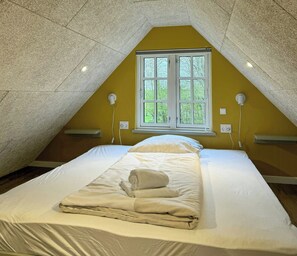 A single bed with white linens and a rolled towel, a window with a view of trees, and a textured ceiling. - Nature retreat with sauna in Ho (Blåvand)