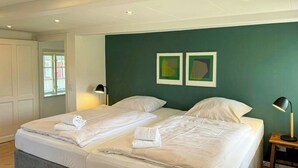 Cama doble con ropa de cama y toallas blancas, mesita de noche con lámpara y pared de acento verde.