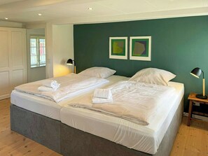 A double bed with white linens and towels, a bedside table with a lamp, and a green accent wall. - Nature retreat with sauna in Ho (Blåvand)