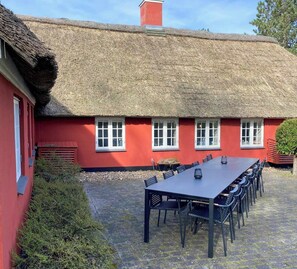 A red building with a thatched roof and a long table with chairs outside. - Nature retreat with sauna in Ho (Blåvand)