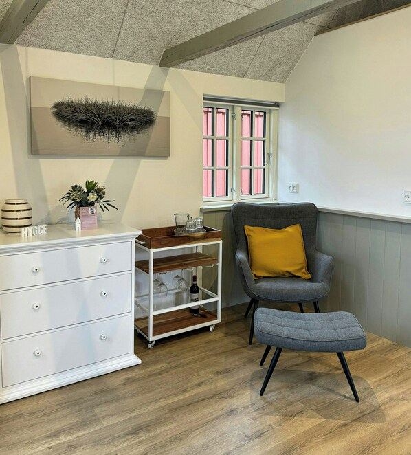 A modern room with a white dresser, a grey armchair with a yellow pillow, a small wooden table, and a wall-mounted artwork. - Nature retreat with sauna in Ho (Blåvand)