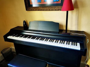 Un piano vertical negro con una lámpara roja y un marco de fotos en la pared.