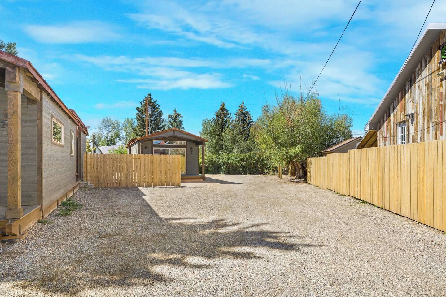 A gravel driveway leading to a wooden fence, a small wooden structure, and a building with a sloped roof.
